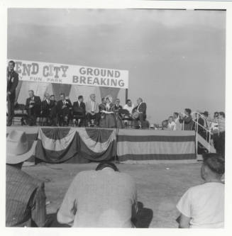 Photograph, people seated on stage at the groundbreaking for Legend City