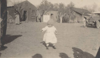 Toddler in yard with buildings and car in background