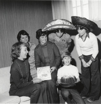 Women and young men gather around a cake