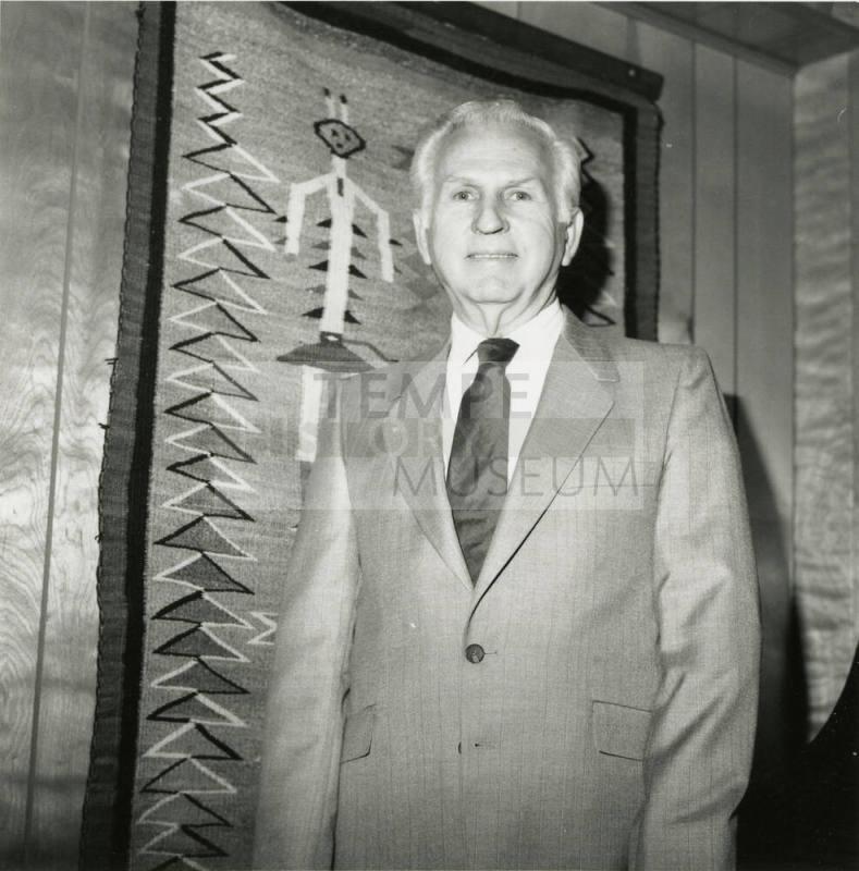 Unknown man standing in front of Native American weaving