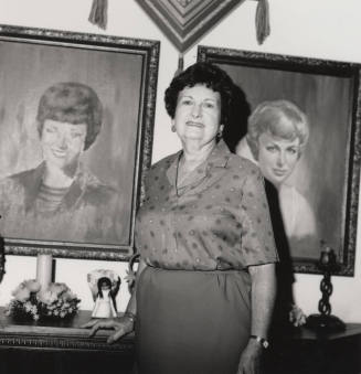 Unidentified woman poses in front of two painted portraits of women