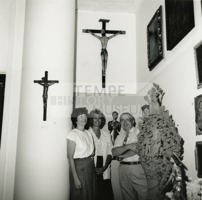 Three unidentified people stand amongst a religious art display