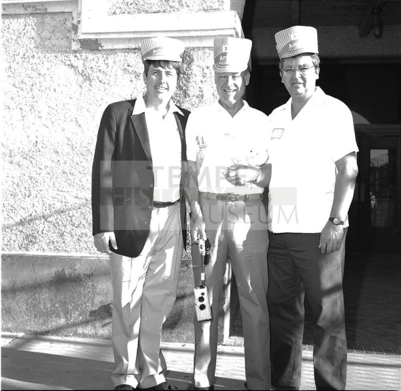 3 men stand outside a concrete building, wearing hats