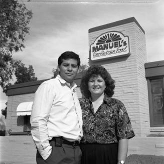 David and Pamela Salazar 27th year of Manuel's Restaurant, standing outside with the sign above their heads