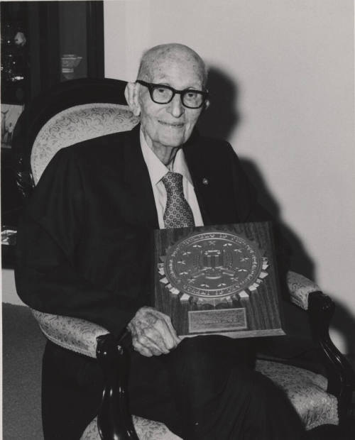 Carl Hayden seated holding large commemorative plaque.