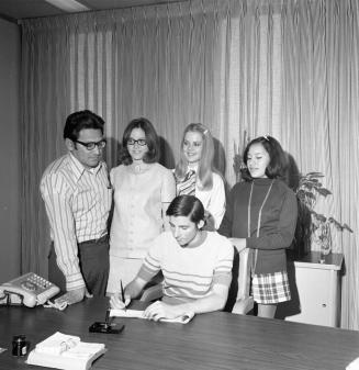Man and 4 young people, one signing paper
