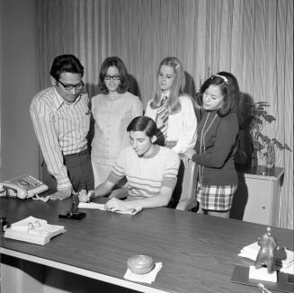 Four people watch teen sign paper