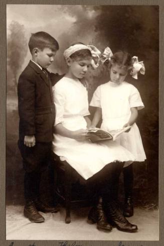 Photo of Everett, Thelma, and Irene Cummins reading a book