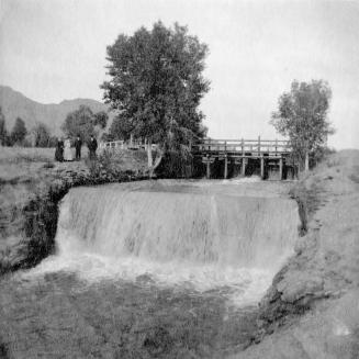 People standing by canal with waterfall and gates.