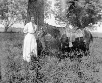 Woman standing by tree with horse