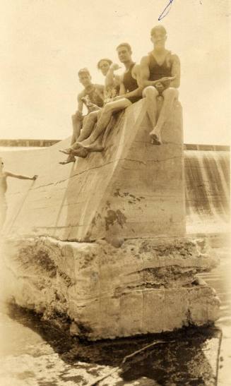 Four men in bathing suits sit on a concrete part of Granite Reef Dam