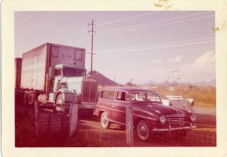 Picture of a late 50s Station Wagon in front of a comercial truck