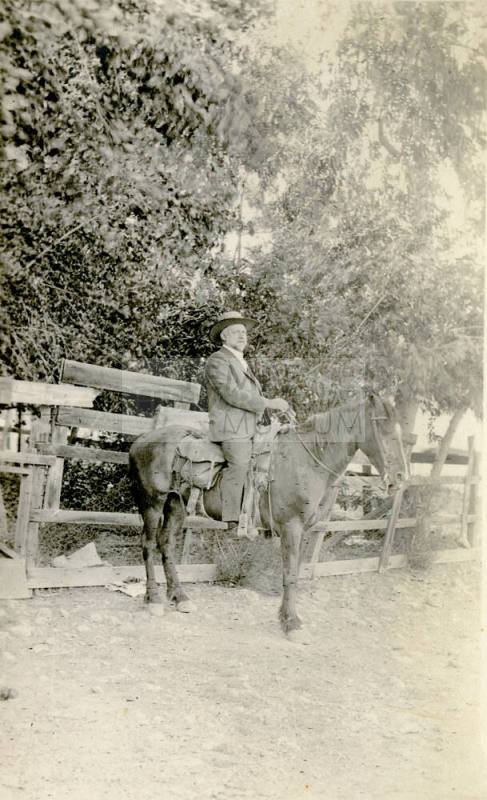 Dr. Fenn J Hart on horseback in front of a chicken-wire fence