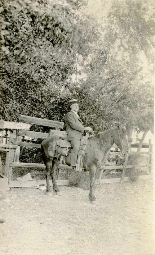 Dr. Fenn J Hart on horseback in front of a chicken-wire fence