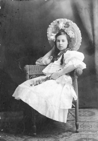Individual portrait of a preteen Mildred Muriel Hart seated in wicker chair