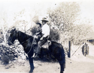Dr. Fenn J Hart atop a dark horse with small child named Bobby