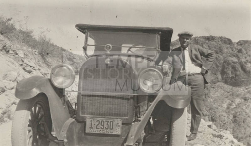 Photo- man standing next to an automobile with a cigar in his right hand