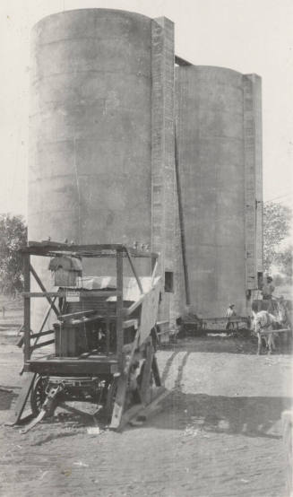 Photo- View of a mobile generator, silos, and  a man driving a horse drawn wagon