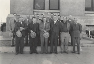 Photo- View of sixteen unidentified men standing in front of a building