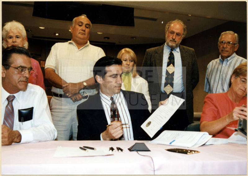 Mayor Neil Giuliano Signing a Paper While City Council Looks On.