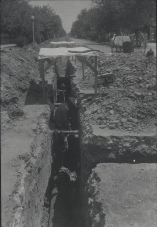 Workmen Lay Pipe in Streetside Trench