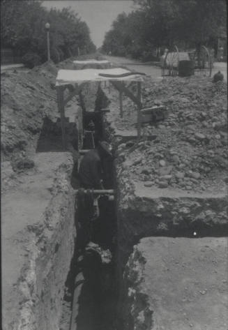 Workmen Lay Pipe in Streetside Trench
