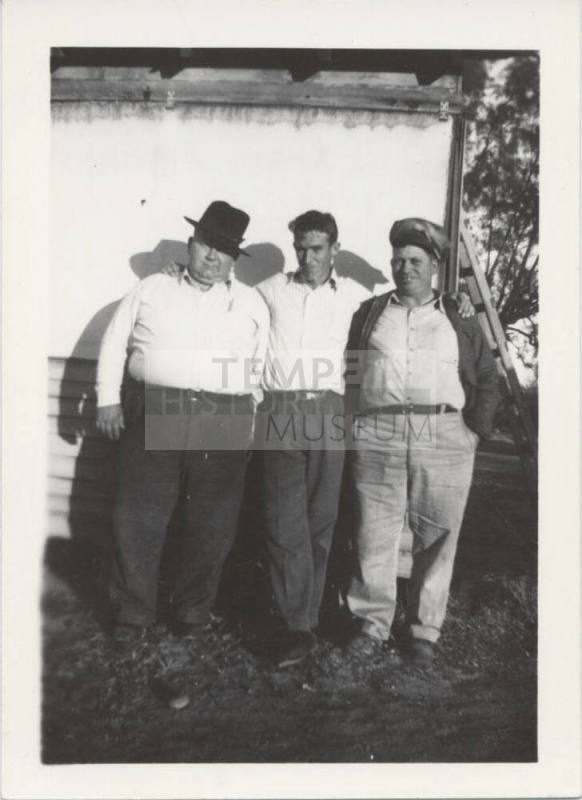 Three Men Standing Against a White Wall