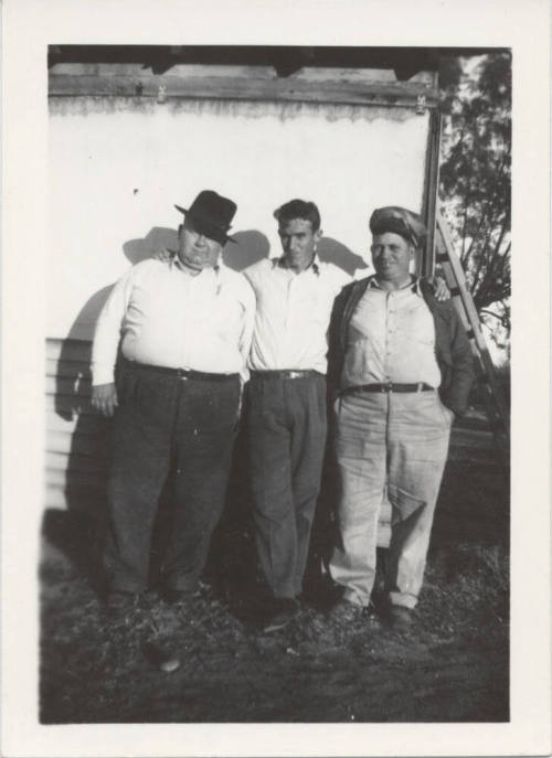 Three Men Standing Against a White Wall