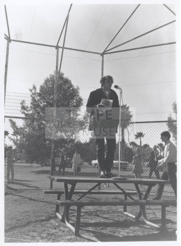 Draft protest march--Man in coat/levi's standing on table with microphone