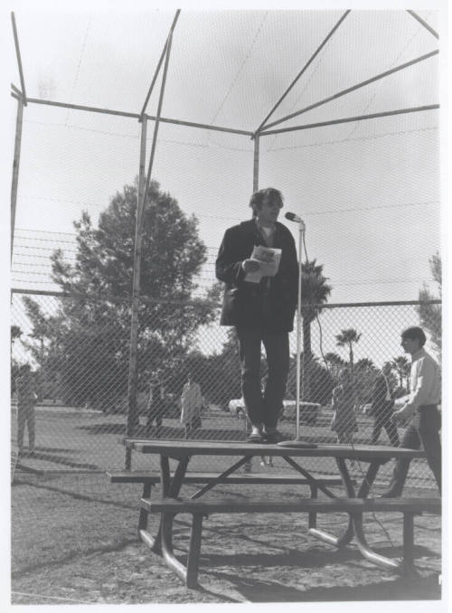 Draft protest march--Man in coat/levi's standing on table with microphone