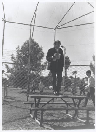 Draft protest march--Man in coat/levi's standing on table with microphone