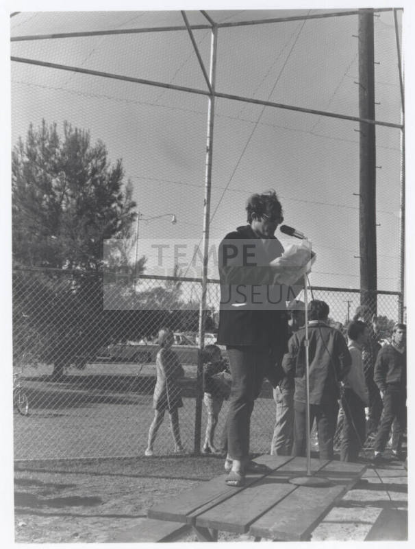 Draft protest march -- Man in coat/levi's standing on table with microphone
