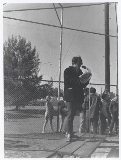 Draft protest march -- Man in coat/levi's standing on table with microphone