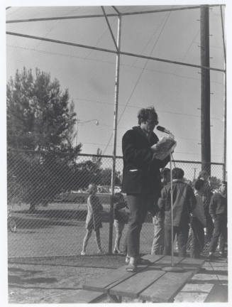 Draft protest march -- Man in coat/levi's standing on table with microphone