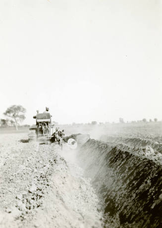 Rear View of Tractor Pulling Ditch Plow