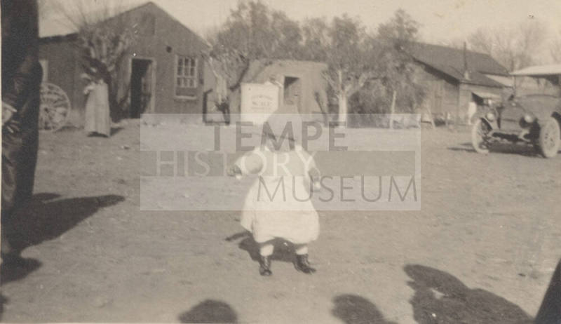 Toddler in yard with buildings and car in background