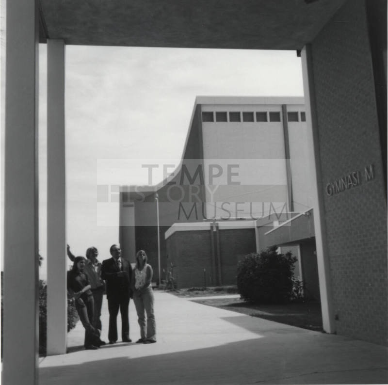 Four people standing near the doorway of a gymnasium, McClintock High School