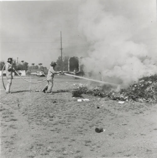 Two Firemen Hose a Smoldering Pile