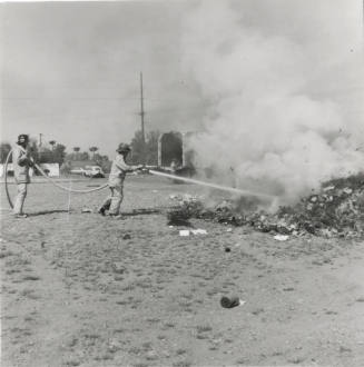 Two Firemen Hose a Smoldering Pile