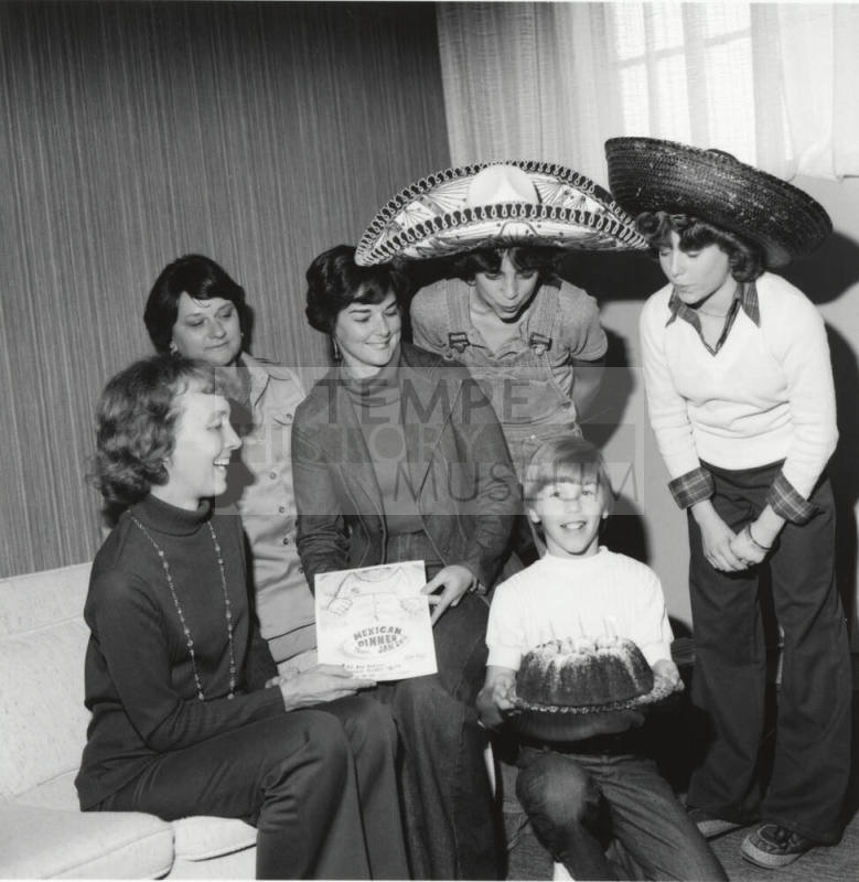 Women and young men gather around a cake