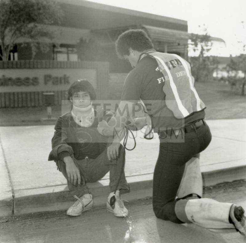 Paramedic attends to an injured young man in a neck brace on a curb