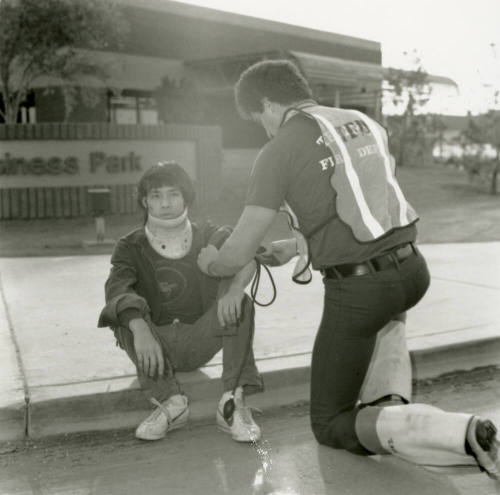 Paramedic attends to an injured young man in a neck brace on a curb