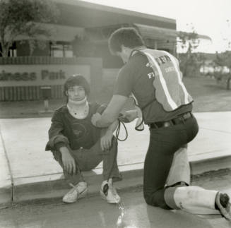 Paramedic attends to an injured young man in a neck brace on a curb