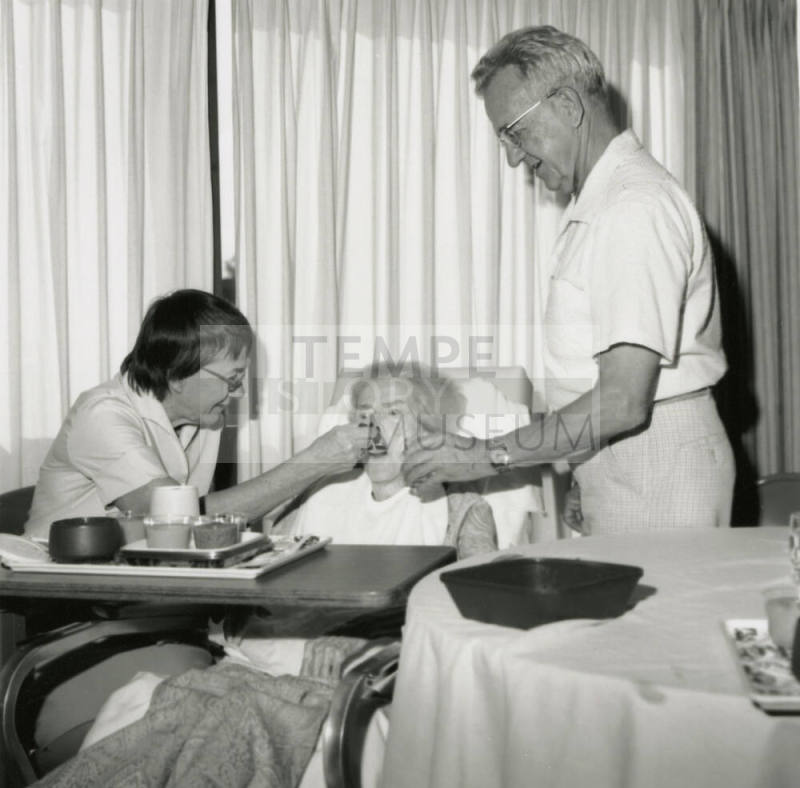 Man and woman feed ill elderly woman in a hospital bed, January 21-27, 1985