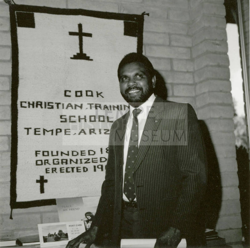 Unidentified man in front of a Cook Christian Training School banner