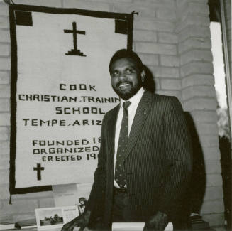 Unidentified man in front of a Cook Christian Training School banner