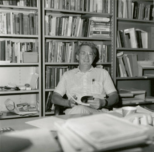 Unidentified man at desk amid bookcases