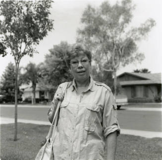 Woman in glasses stands in the front yard of a residential neighborhood