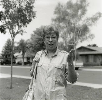 Woman in glasses stands in the front yard of a residential neighborhood