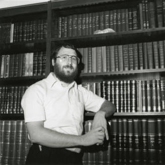 Unidentified Man Stands Next To Bookshelves